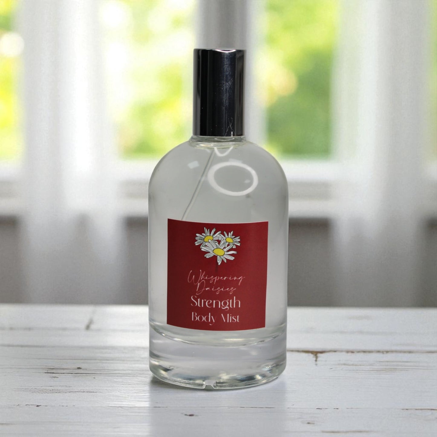 Bottle of 'Whispering Prairie Strength Body Mist' on a wooden surface with a blurred window background.